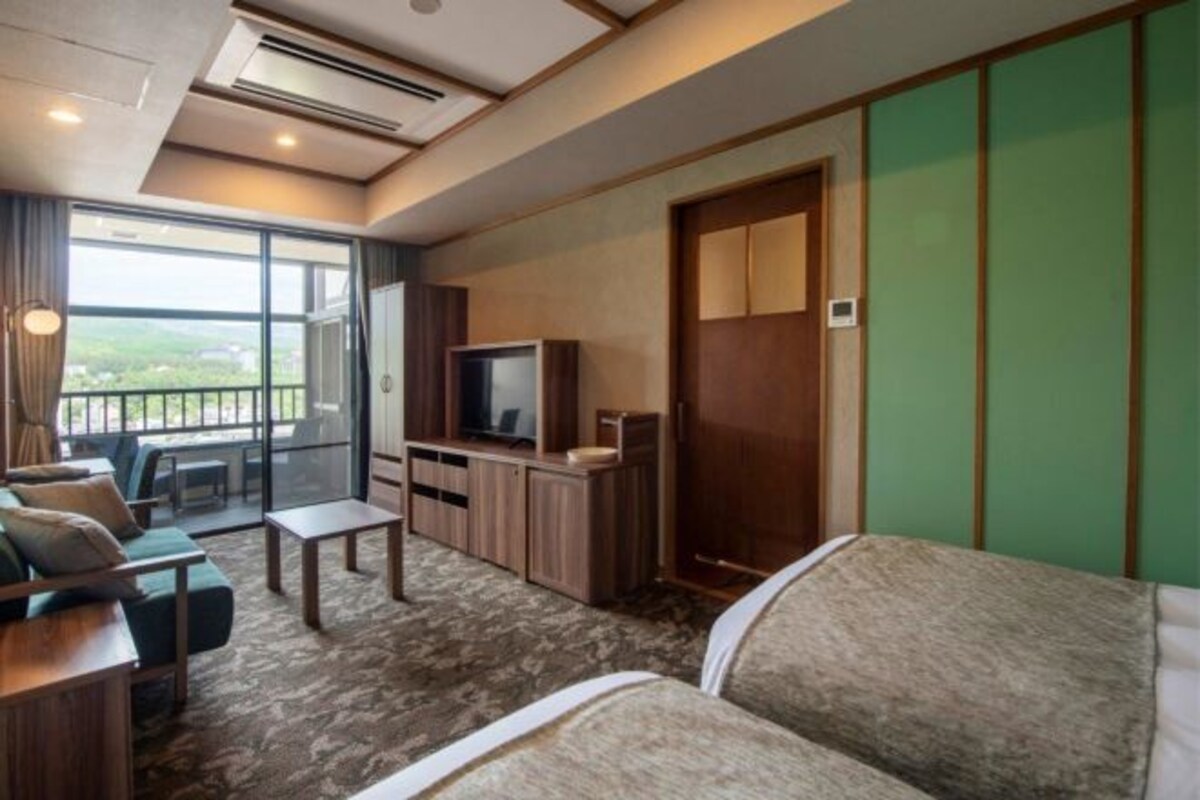 Habitación de hotel con sofá, televisión, mesita, armario y ropero.