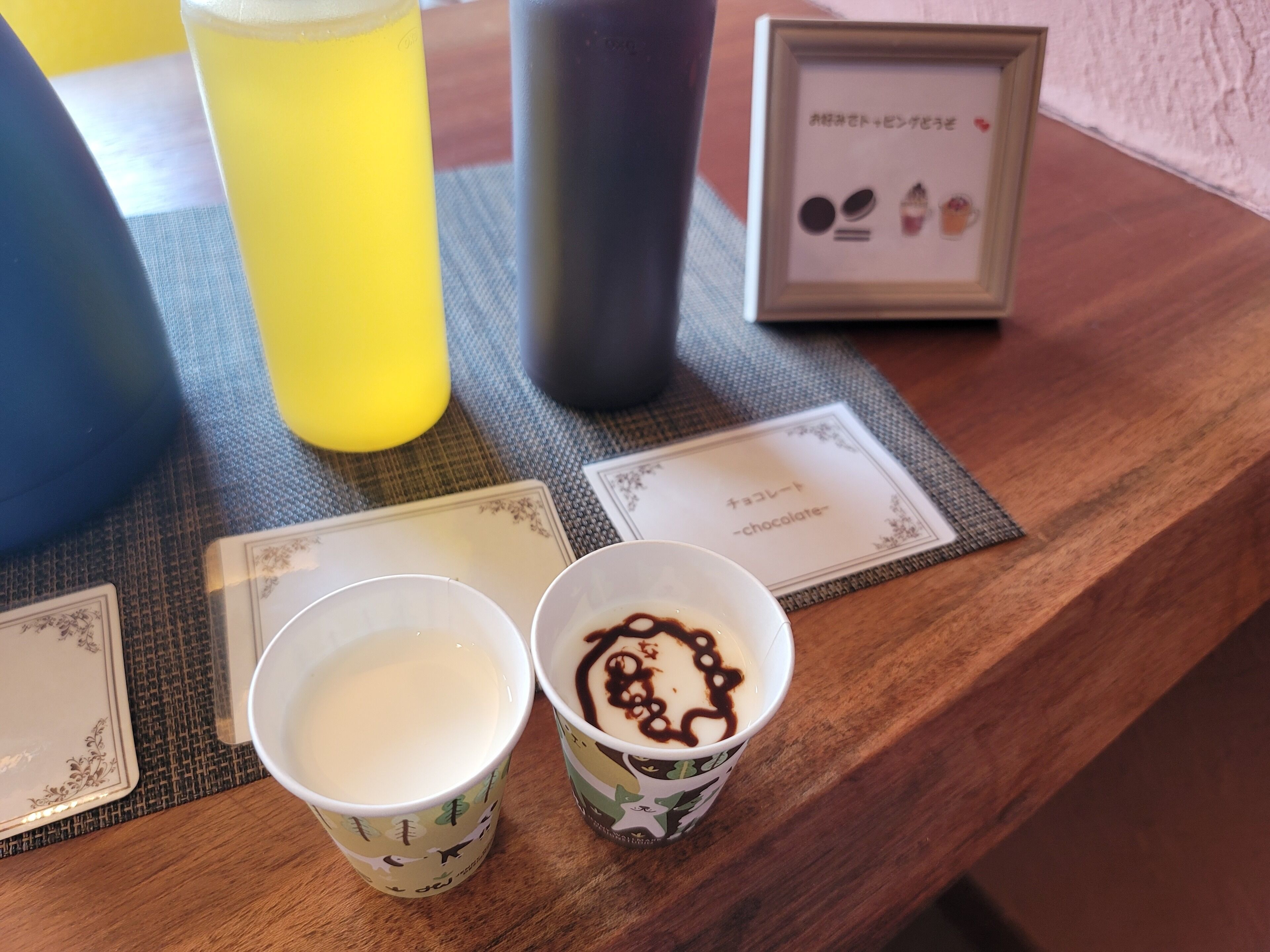 Ein Tisch mit zwei Kaffeetassen, eine mit Milch und die andere mit Schokoladensirup, sowie einer gerahmten Speisekarte darauf.
