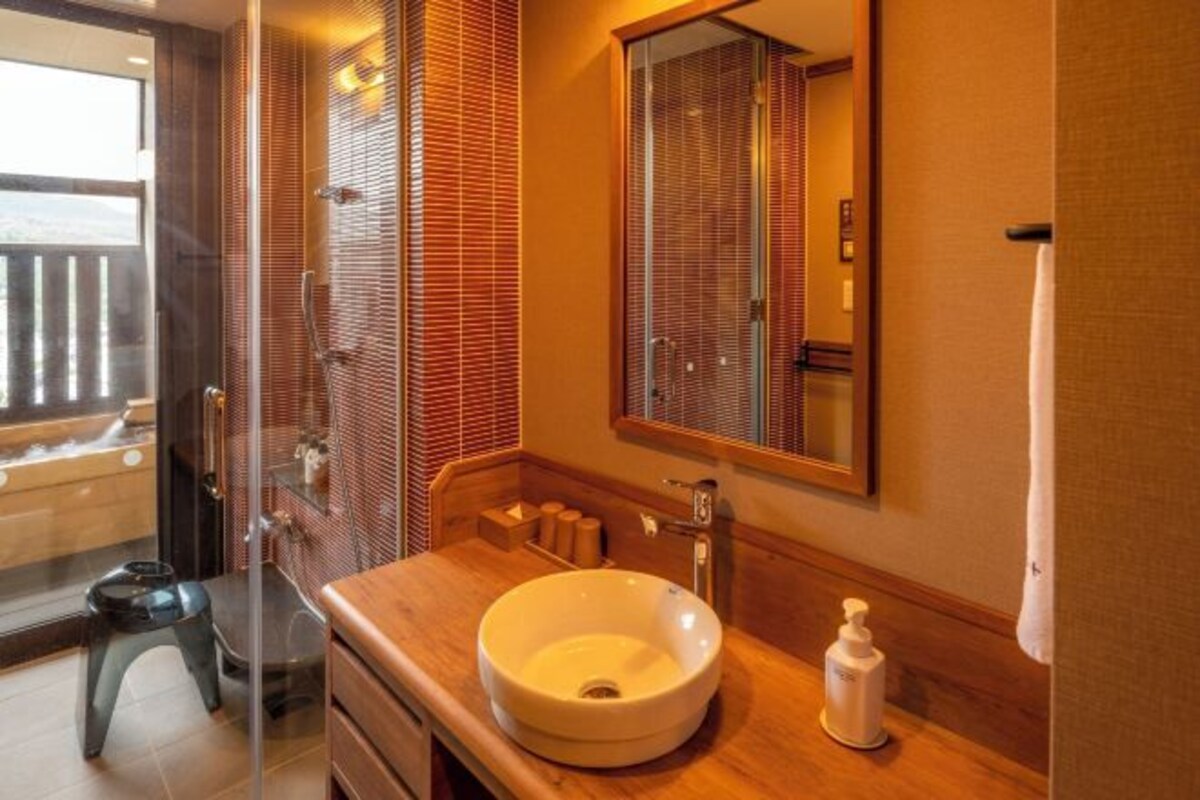 Un baño con ducha de vidrio, tocador de madera, un espejo grande y vistas a un balcón.