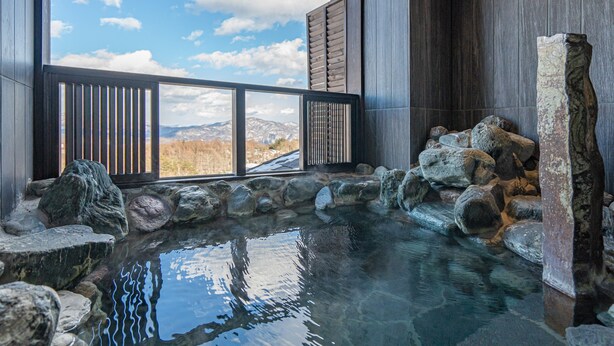 Un jacuzzi de piedra con vistas a montañas a través de una barandilla de madera.