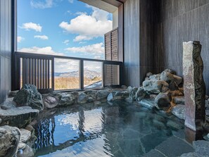 A stone hot tub with a view of mountains through a wooden railing. - La Vista Kusatsu Hills (Kusatsu)