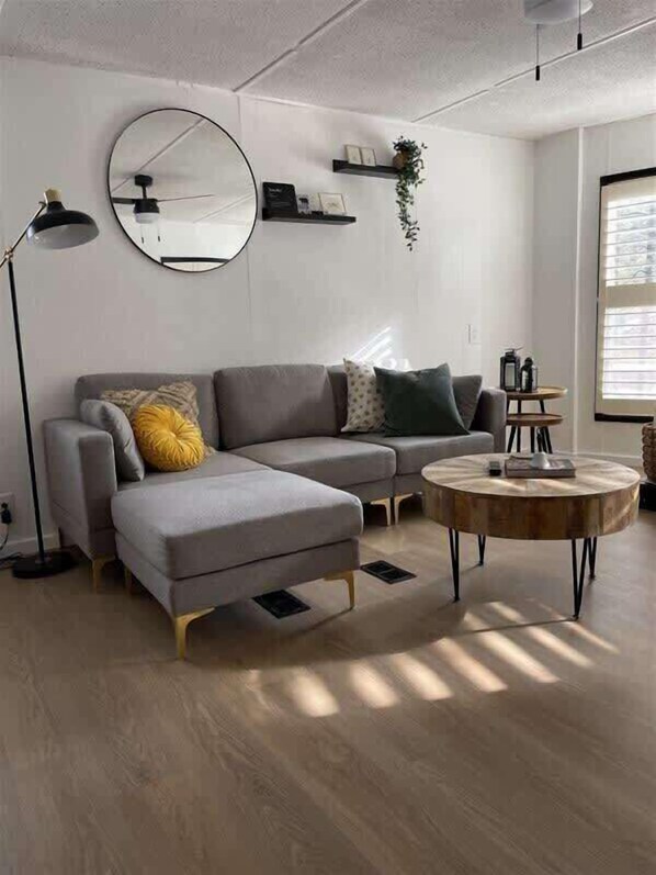 A modern living room with a grey sectional sofa, a round coffee table, and a large mirror on the wall.