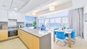 A modern kitchen with a central island, a dining area with blue chairs, and large windows offering a view of the city.