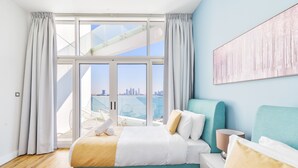A hotel room with a large window, a bed, a bedside table, and a view of a cityscape.