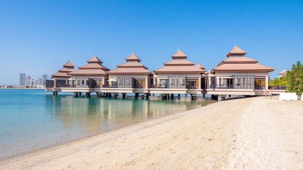 A beachfront resort with overwater bungalows, a sandy beach, and a clear blue sky.