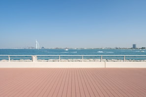 A wooden deck with a railing overlooking a body of water, a distant city skyline, and a prominent sail-shaped structure.