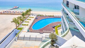 A modern hotel with a pool, beach view, and a curved glass balcony.