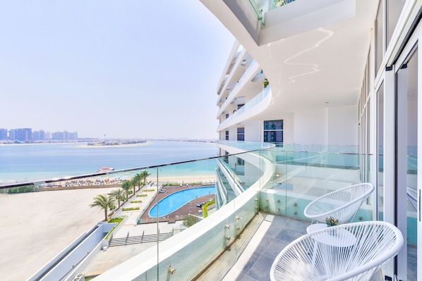 A high-rise hotel with a glass balustrade overlooking a beach and a pool.