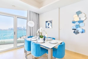 A modern dining area with a white table set for four, blue chairs, and a view of the city through large windows.