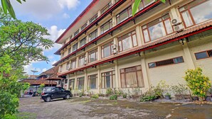 A multi-story building with a tiled roof, large windows, and air conditioning units. There is a car parked in front and a small garden area with potted plants. - Super OYO 91870 Warna Kedaton (Denpasar)