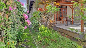 A garden with various plants and flowers, a wooden pergola, and a seating area with chairs and a table. - Super OYO 91870 Warna Kedaton (Denpasar)
