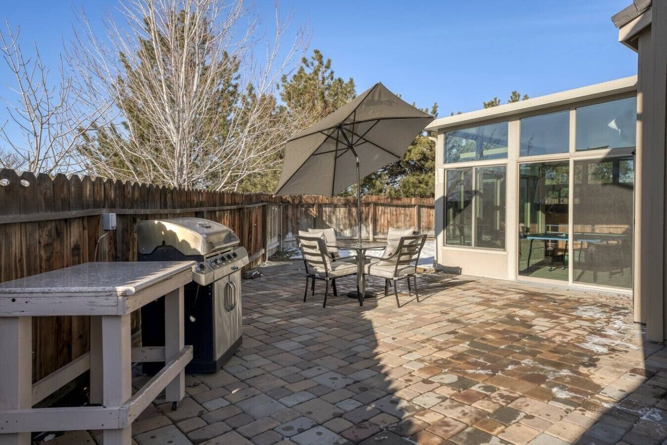 Patio con barbecue, tavolo da esterno, sedie e ombrellone.
