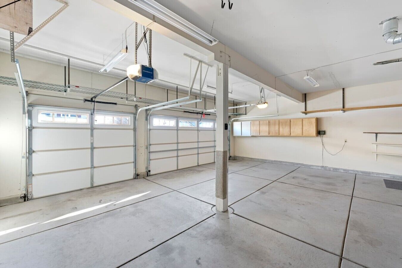 Uma garagem espaçosa com chão de concreto, portas de metal e iluminação por cima.