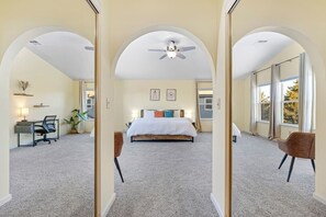 Een slaapkamer met een bed, een bureau, een stoel en een plafondventilator.
