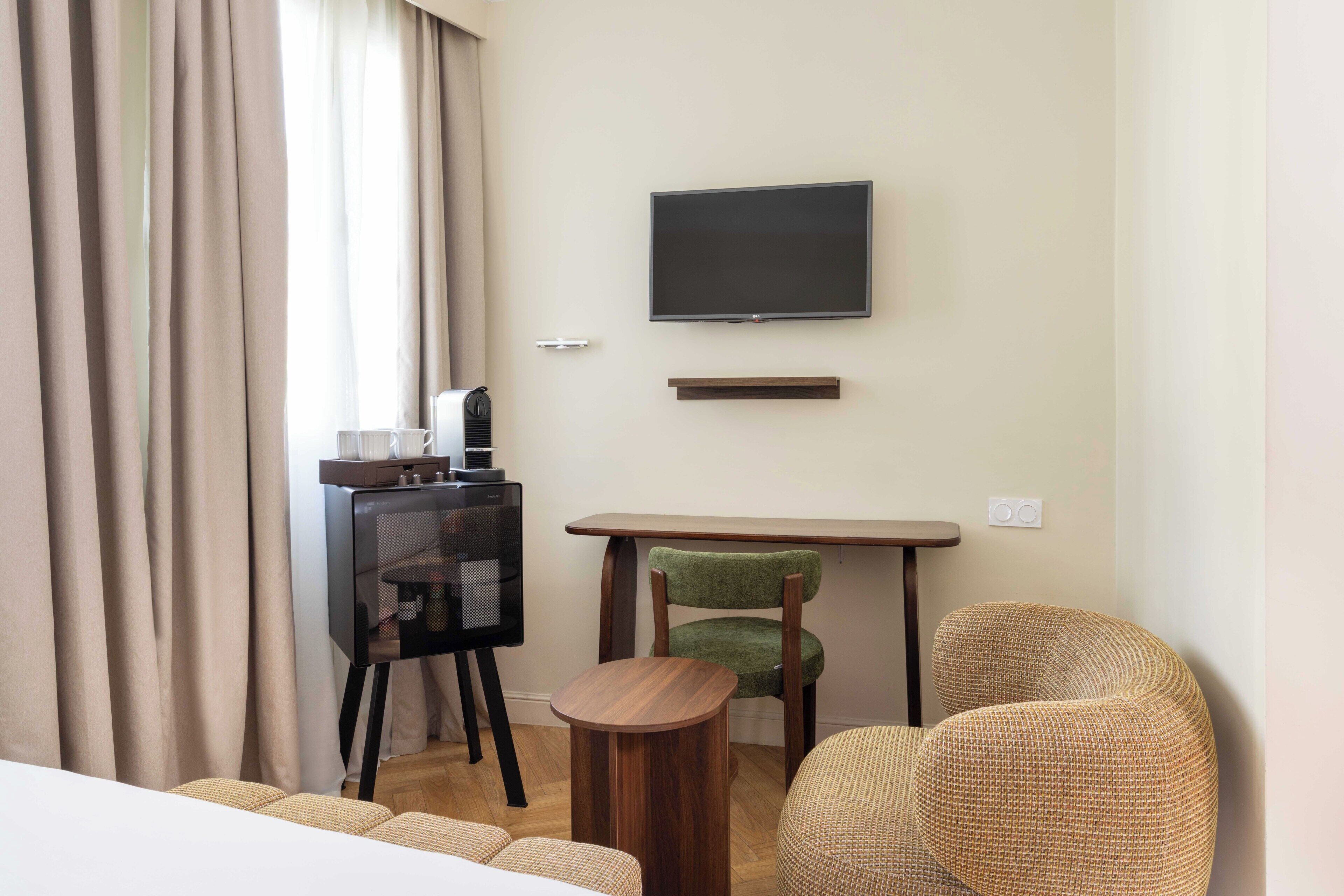 Una habitación de hotel con una cama, un televisor montado en la pared, un escritorio con una silla y una pequeña mesa redonda.