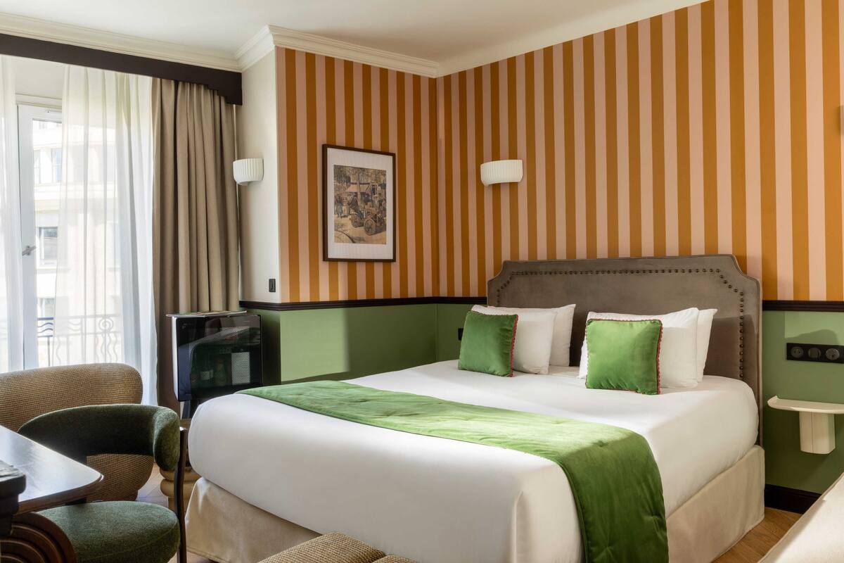 A hotel room with a large bed, a television, a desk, and a chair.