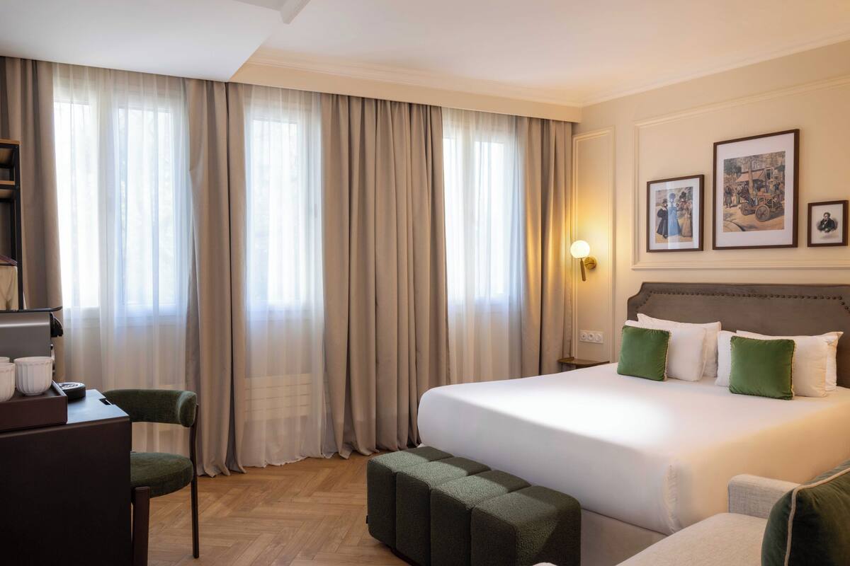 A hotel room with a bed, a desk, a chair, and a large window with curtains.