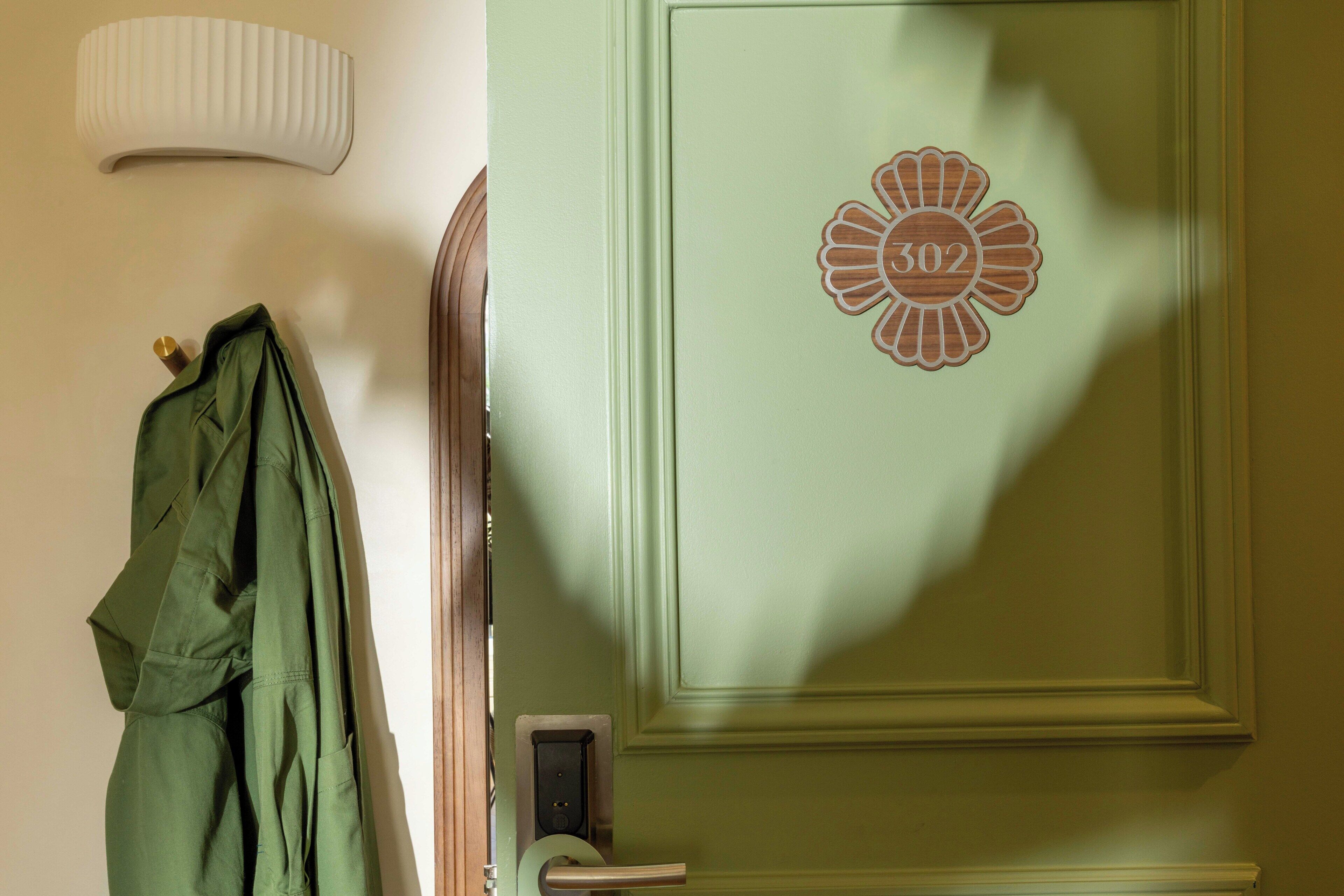 A door with a number plate, a coat hanging on a hook, and a light fixture on the wall.