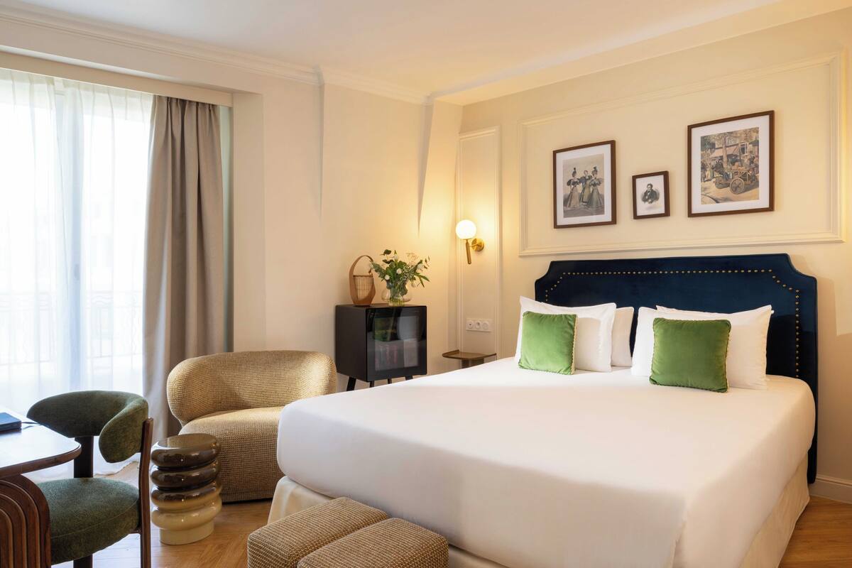 A hotel room with a large bed, a desk, a chair, and a TV.