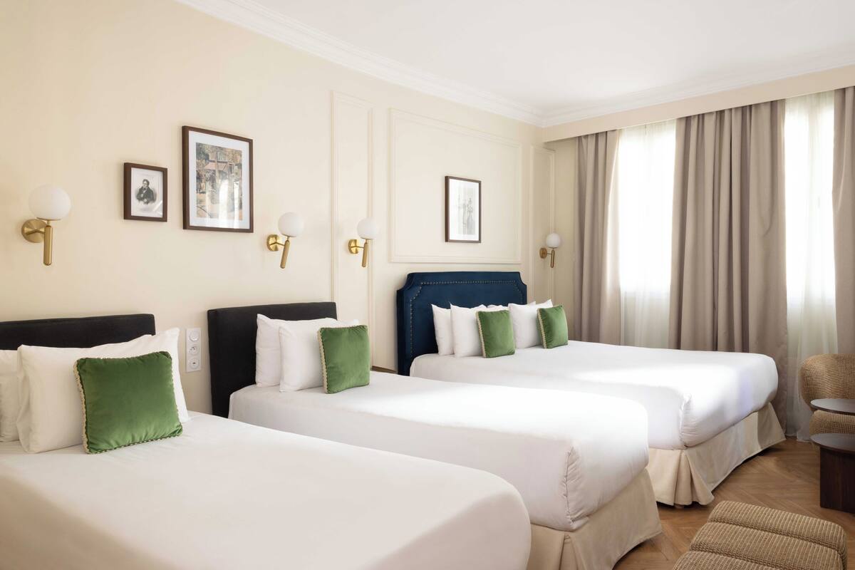 A hotel room with three beds, a chair, and a small table.