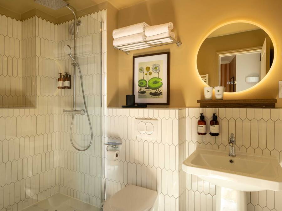Un baño con ducha, inodoro, lavabo y un cuadro enmarcado sobre el espejo.