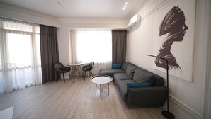 A modern living room with a grey sofa, a round coffee table, and a floor lamp. There is a painting on the wall and a window with curtains. - Cozy 1-Bedroom Apartment in the Heart of Yerevan by Sweet Home (Yerevan)