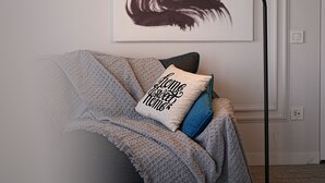 A room with a framed artwork on the wall, a floor lamp, a couch with a throw blanket, and a pillow with text. - Cozy 1-Bedroom Apartment in the Heart of Yerevan by Sweet Home (Yerevan)