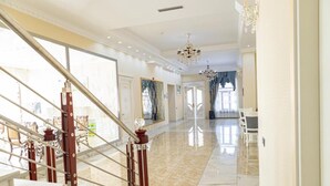 Un'ampia hall dell'hotel con pavimento in marmo, una scalinata con balaustre rosse e un lampadario.