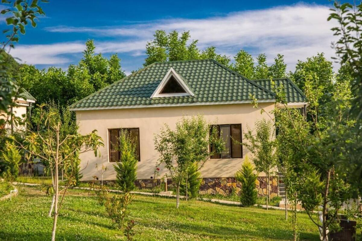 Una casa de un piso con techo de tejas verdes, base de piedra y un ventanal pequeño triangular.