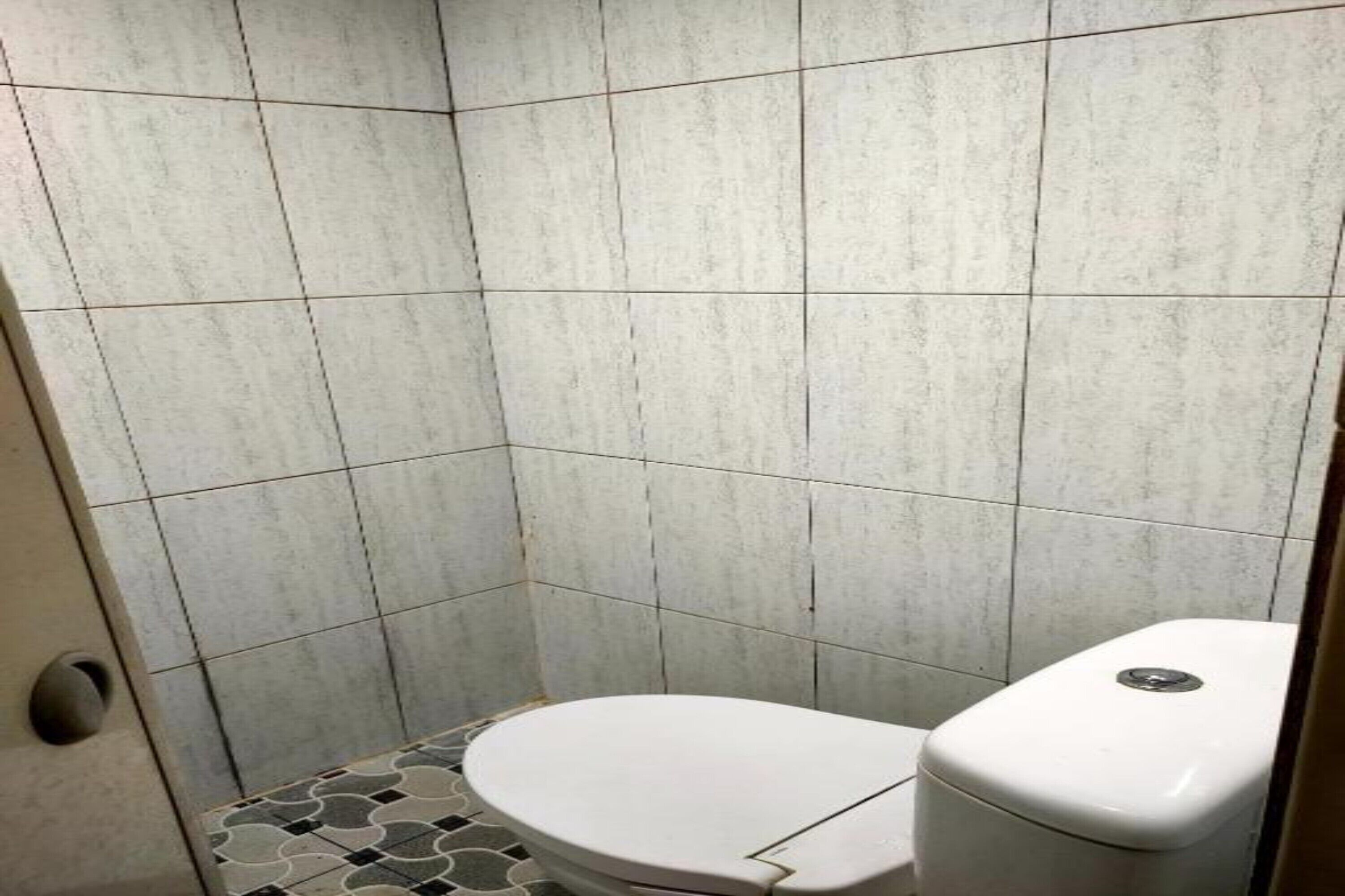 A small, tiled bathroom with a white toilet and a tiled floor.
