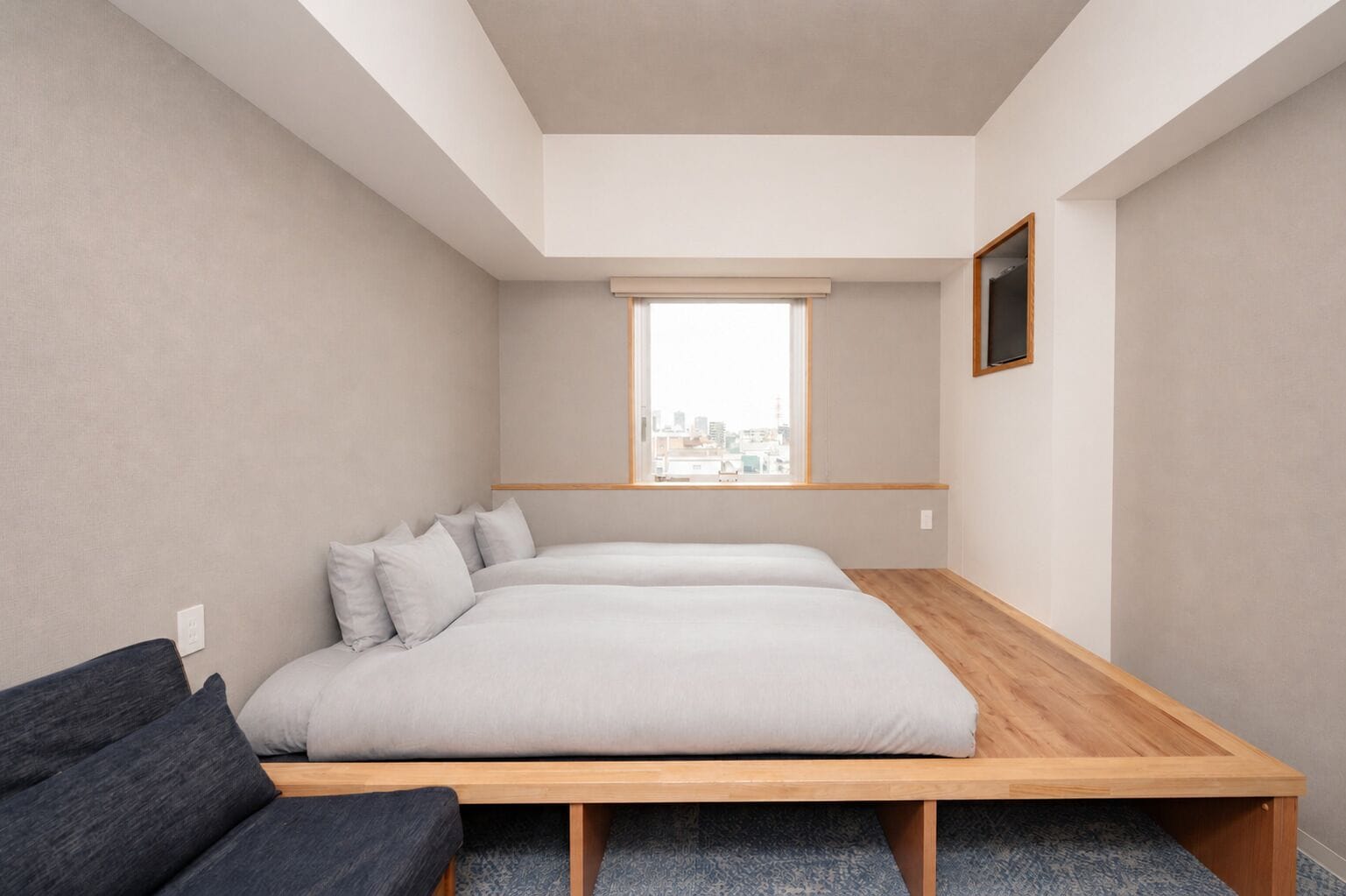 A bedroom with a bed, a bench, a window, and a city view.