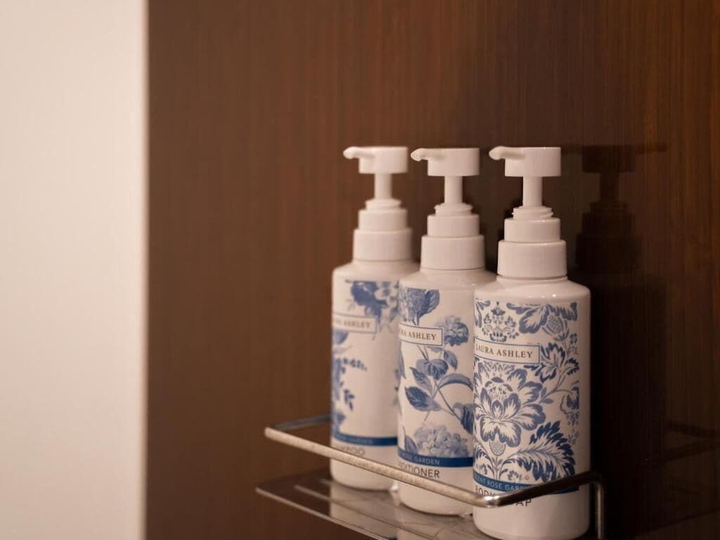 Trois flacons de lotion pour le corps de la marque Laura Ashley, posés sur une étagère.