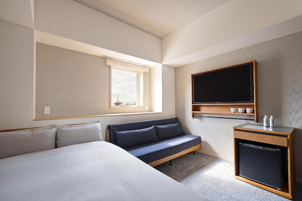 Habitació d'hotel amb un llit, un sofà, una petita televisió i una finestra.