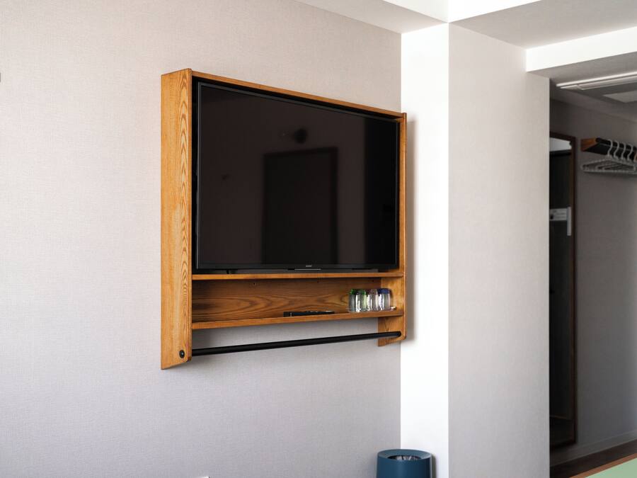 Un televisor de pared con marco de madera, un control remoto negro y una pequeña estantería con botellas.