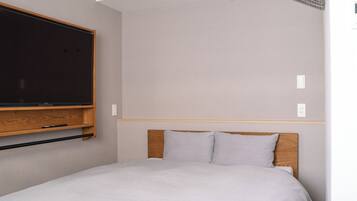 A modern hotel room with a large flat-screen TV mounted on the wall, a wooden headboard, and a simple bed with white bedding.