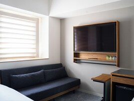 Una habitación de hotel moderna con un sofá azul oscuro, un televisor de pantalla plana montado en la pared, una mesita de madera pequeña y un lavavajillas empotrado.