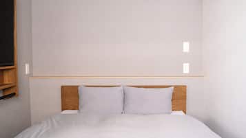 A simple, clean room with a bed, wooden headboard, and a light-colored wall.