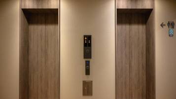An elevator with a control panel, a wheelchair accessibility sign, and a directional arrow sign.