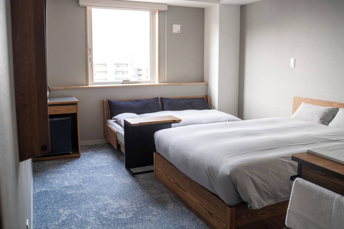 A compact hotel room with a single bed, a small desk, and a window providing a view of the cityscape.