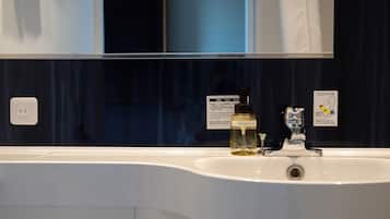 Un baño con un lavamanos blanco, un espejo y una pared azul oscuro. Hay un cartel con texto en japonés y una botella de jabón para manos.