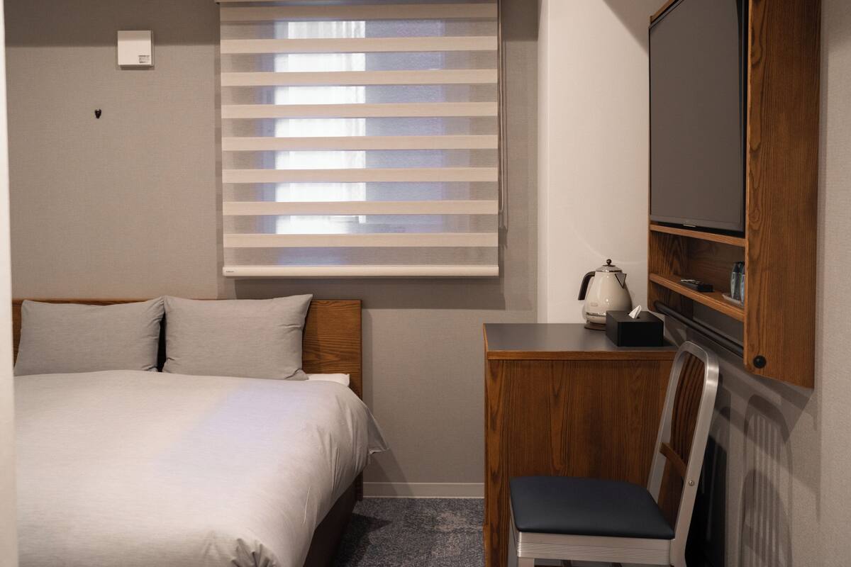 A hotel room with a bed, a desk, a chair, a television, and a window with blinds.