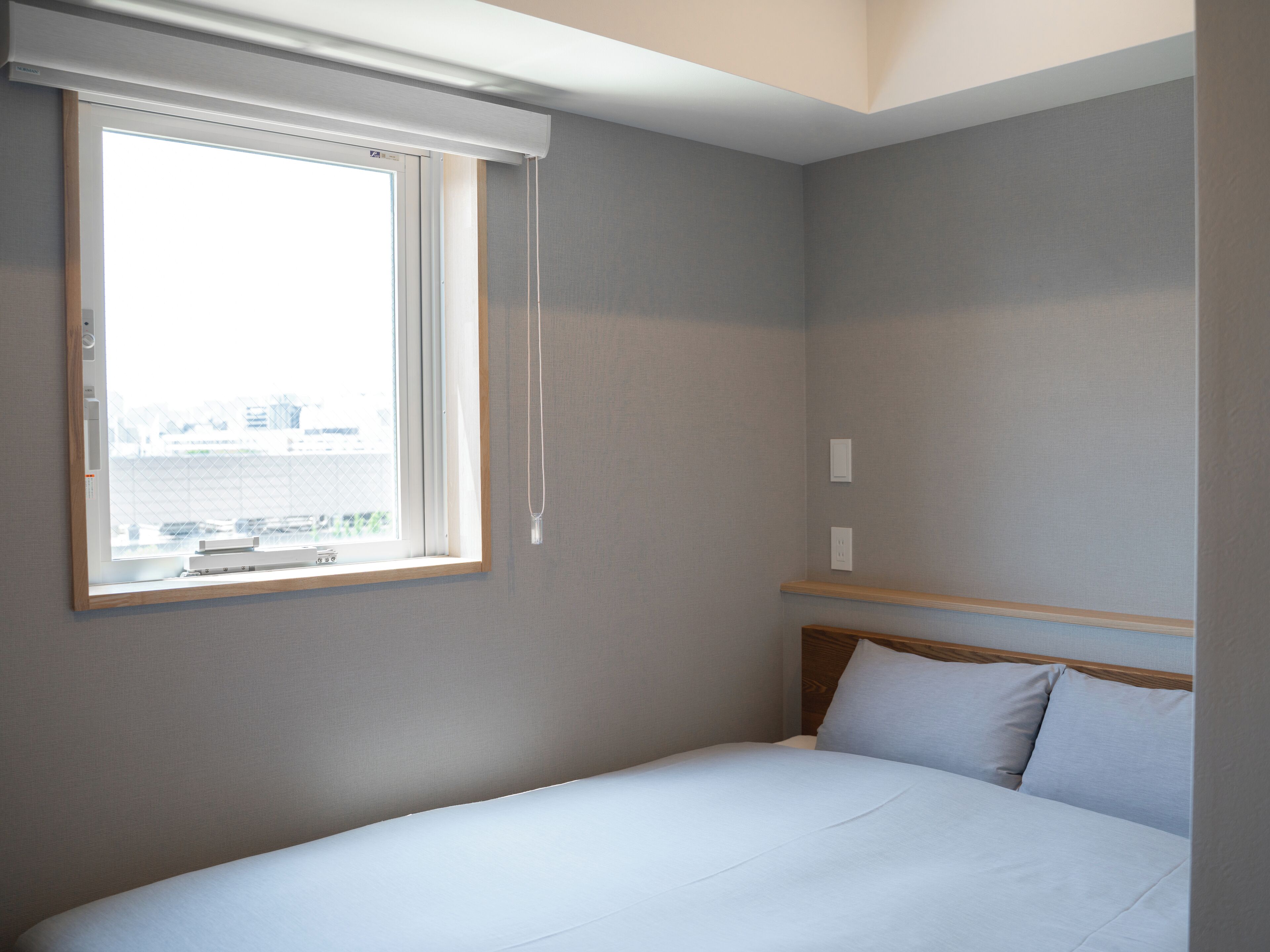 Una habitación de hotel con cama, ventana con persianas y vistas a la ciudad.
