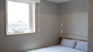 Una habitación de hotel con cama, ventana con persianas y vistas a la ciudad.