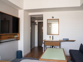 Una habitación de hotel moderna con un televisor de pantalla plana grande, un tocador de madera con espejo, una mesita pequeña y un sofá.