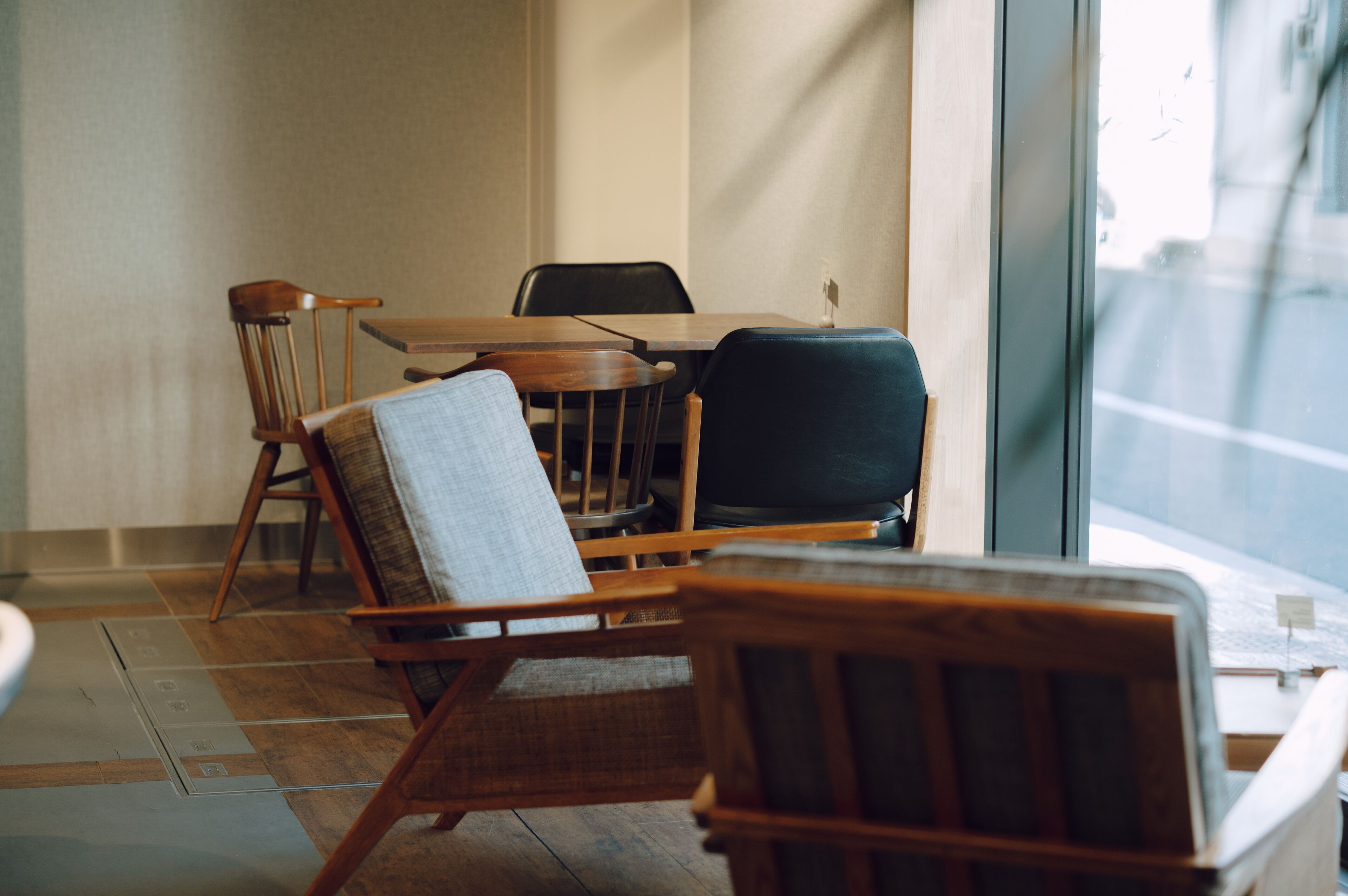 A dining area with wooden chairs and a table, a window with a view of the street, and a tiled floor.