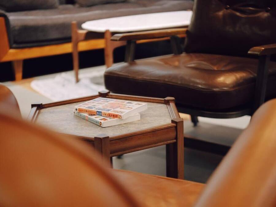 Una sala de estar acogedora con un sillón de cuero, una mesita de centro de madera con un libro y una mesita auxiliar blanca.