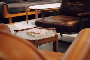 Una sala de estar acogedora con un sillón de cuero, una mesita de centro de madera con un libro y una mesita auxiliar blanca.