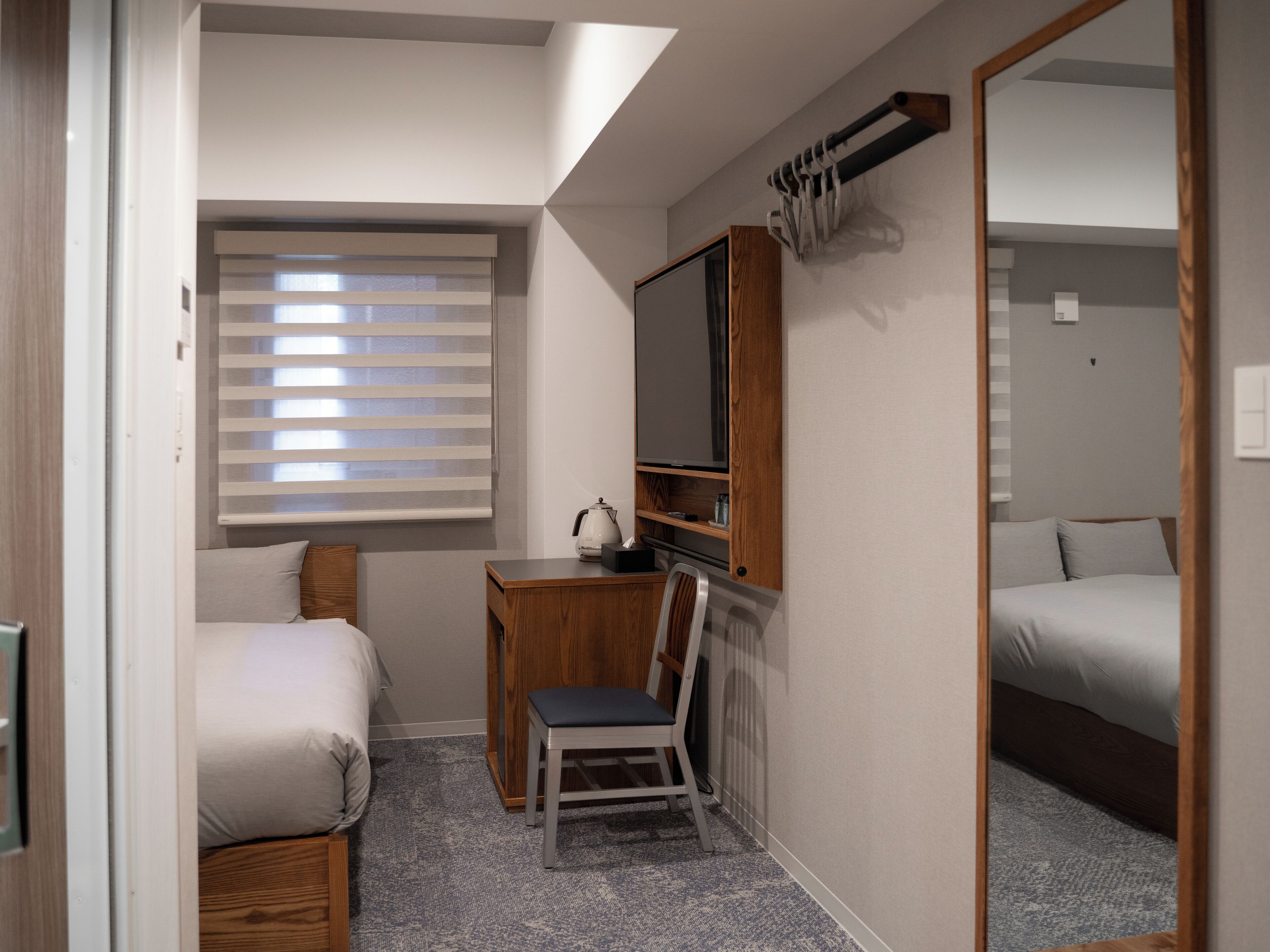 A compact bedroom with a bed, a desk with a chair, a television, and a mirror.
