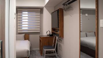 A compact bedroom with a bed, a desk with a chair, a television, and a mirror.
