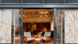A modern interior with a seating area featuring two armchairs and a small table, a wooden floor, and a brick wall. - OTHER SPACE Asakusa (Tokyo)